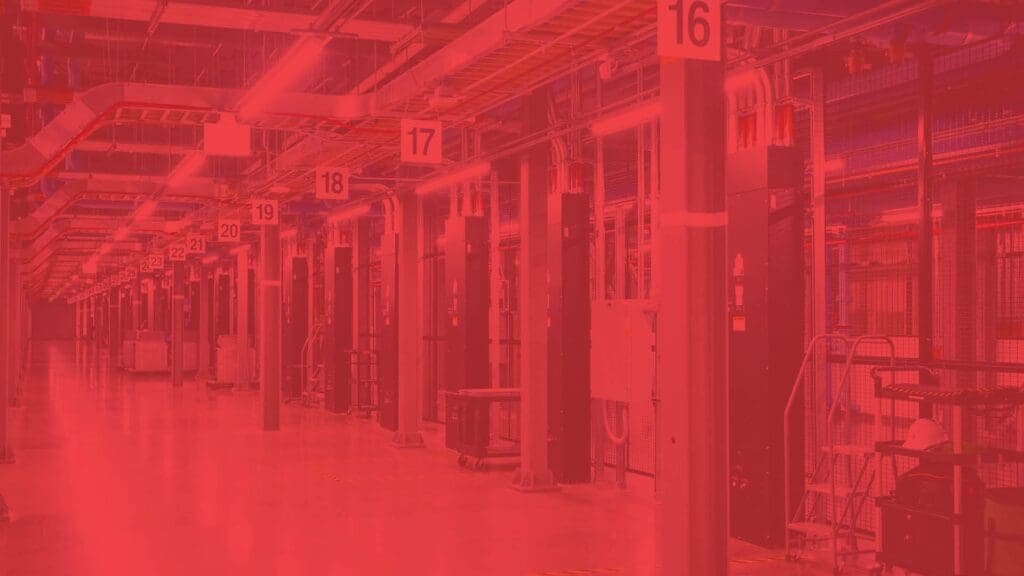 A long hallway in the Tilden technical facility, with numbered columns and industrial equipment, bathed in red lighting.