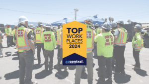 A group of construction workers in safety vests and helmets stands together outside. A sign in the middle reads "Top Workplaces Arizona 2024" by azcentral, celebrating DP Electric's achievement.