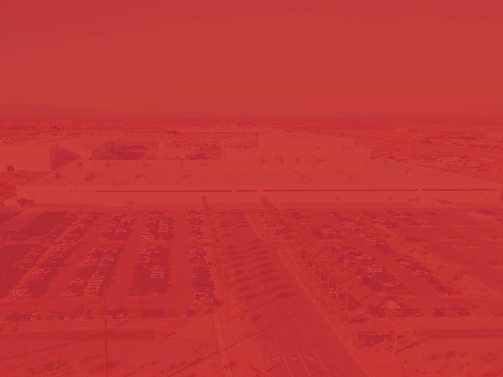 An aerial view of a large, confidential industrial facility with a parking lot full of cars in front and a surrounding desert landscape, overlaid with a red filter.