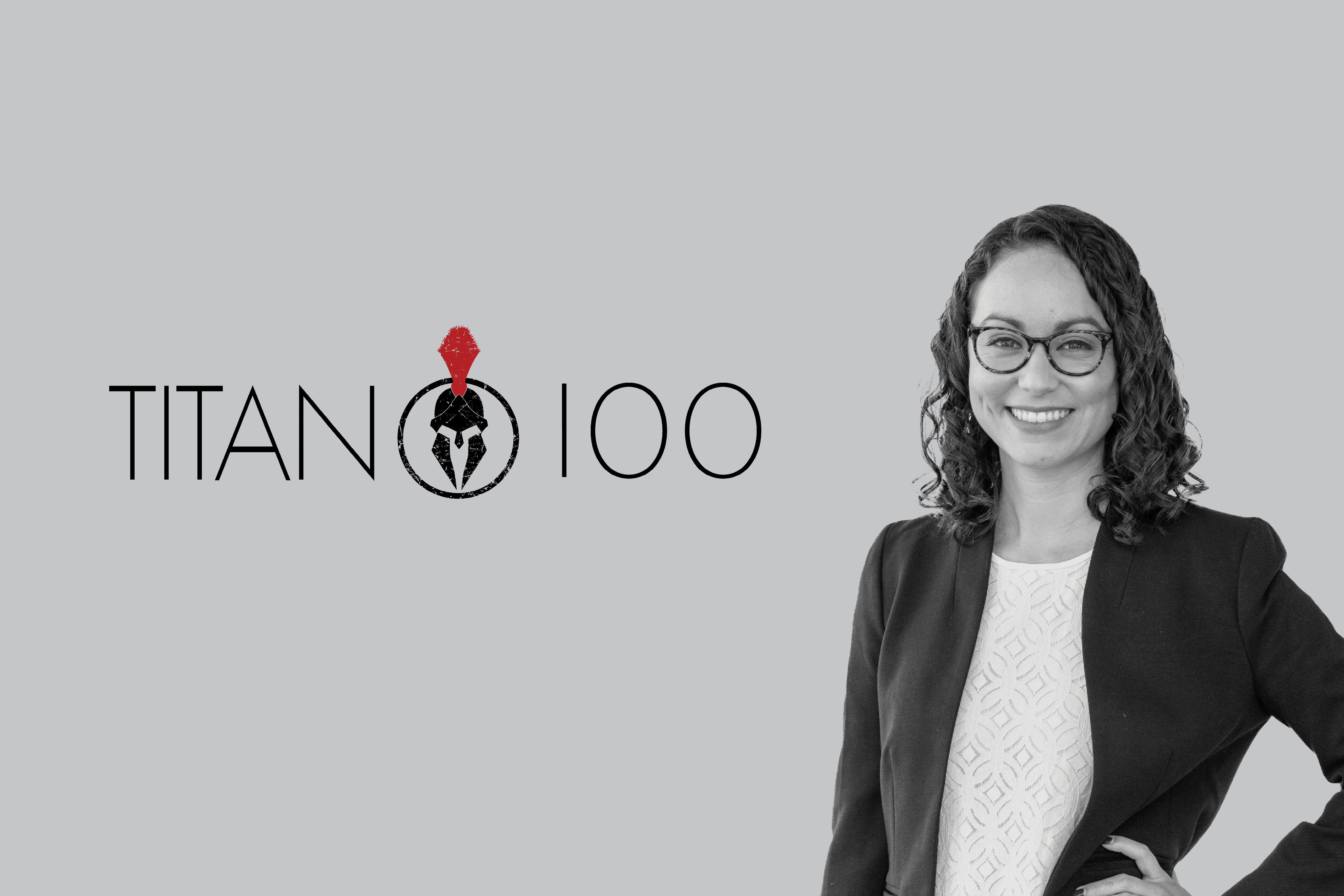 A woman in a business suit and glasses stands with her hand on her hip, smiling. Next to her is the 'Phoenix Titan 100' logo featuring a helmeted figure. The background is grey.